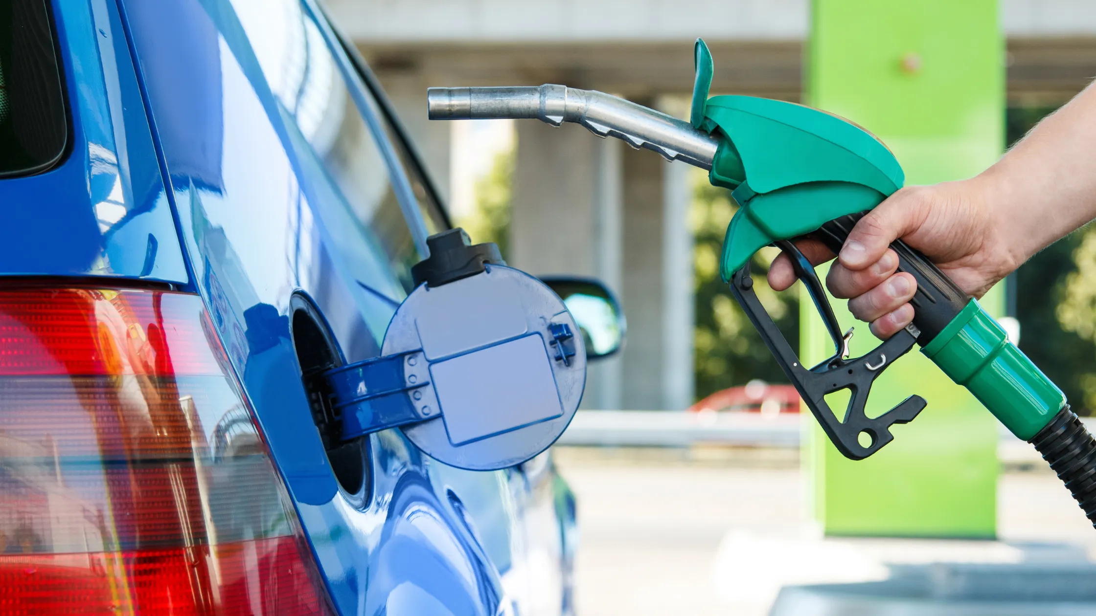 una-mano-sosteniendo-una-pistola-de-gasolina-verde-frente-al-tanque-abierto-de-un-automovil-azul
